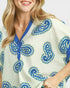 Woman wearing a white dress with blue paisley patterns on a plain background