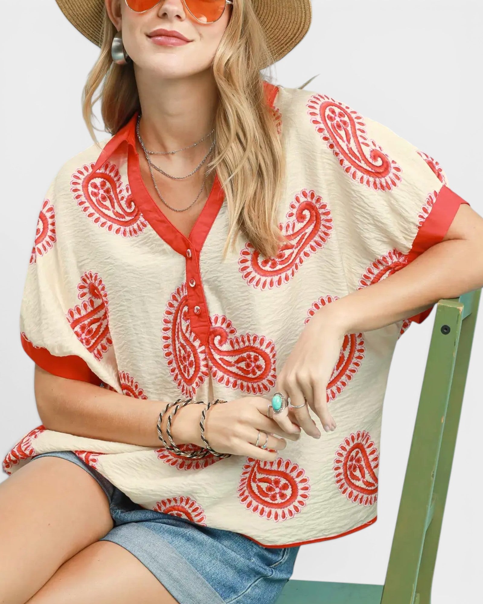 Woman wearing a red and white patterned top with a straw hat and sunglasses.