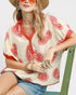 Woman wearing a red and white patterned top with a straw hat and sunglasses.