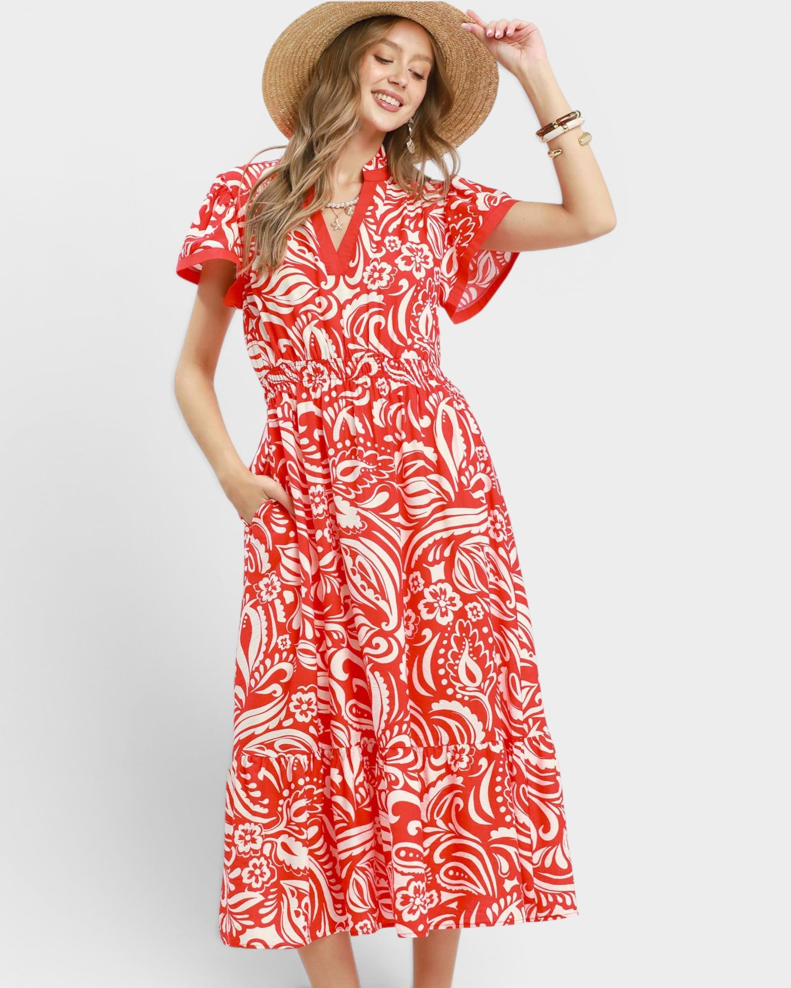Woman wearing a red and white patterned dress with a straw hat on a white background
