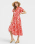 Woman wearing a red and white patterned dress with a straw hat on a white background