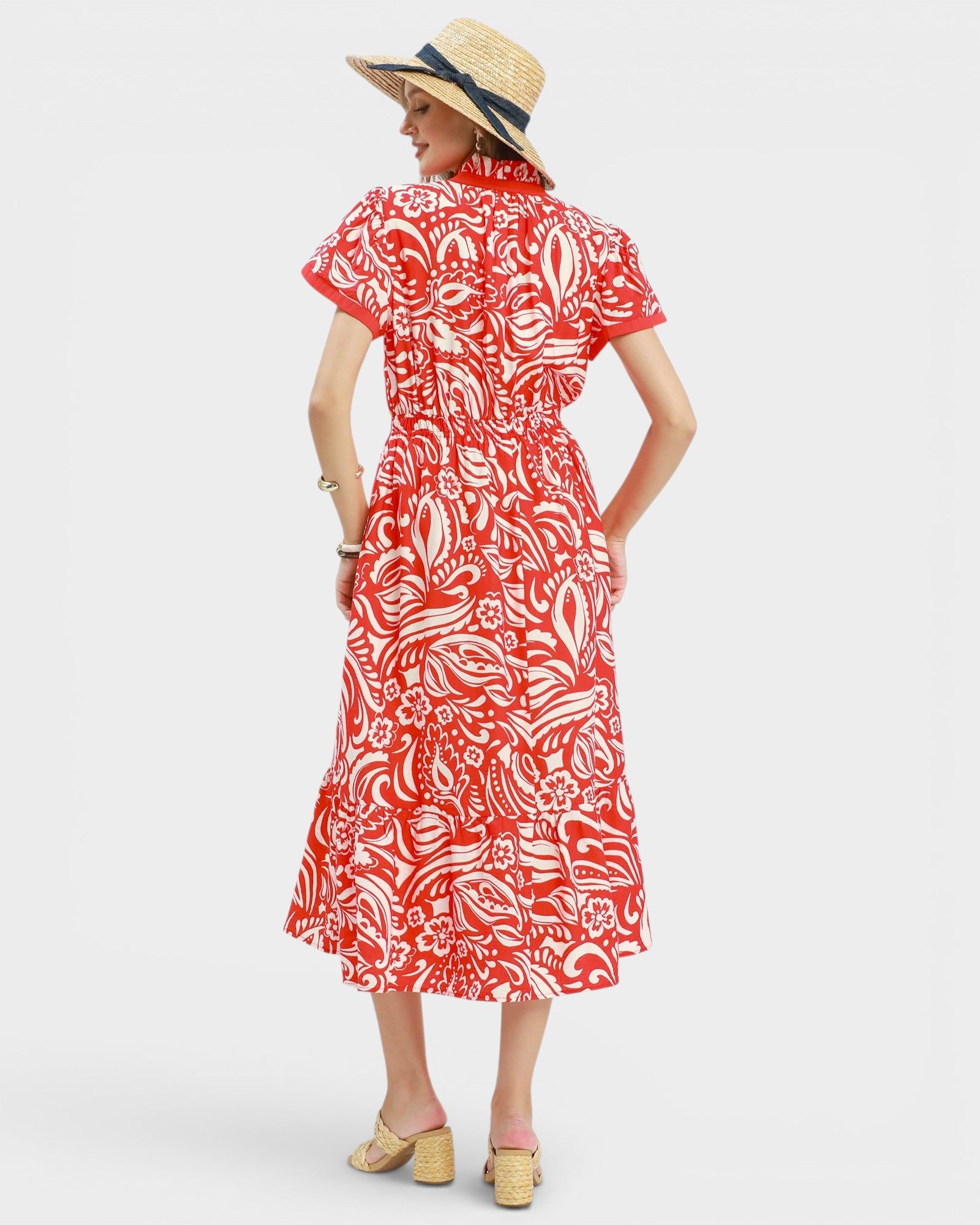 Woman wearing a red and white patterned dress with a straw hat on a light gray background