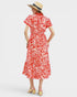 Woman wearing a red and white patterned dress with a straw hat on a light gray background