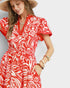Woman wearing a red and white patterned dress with a straw hat on a light gray background