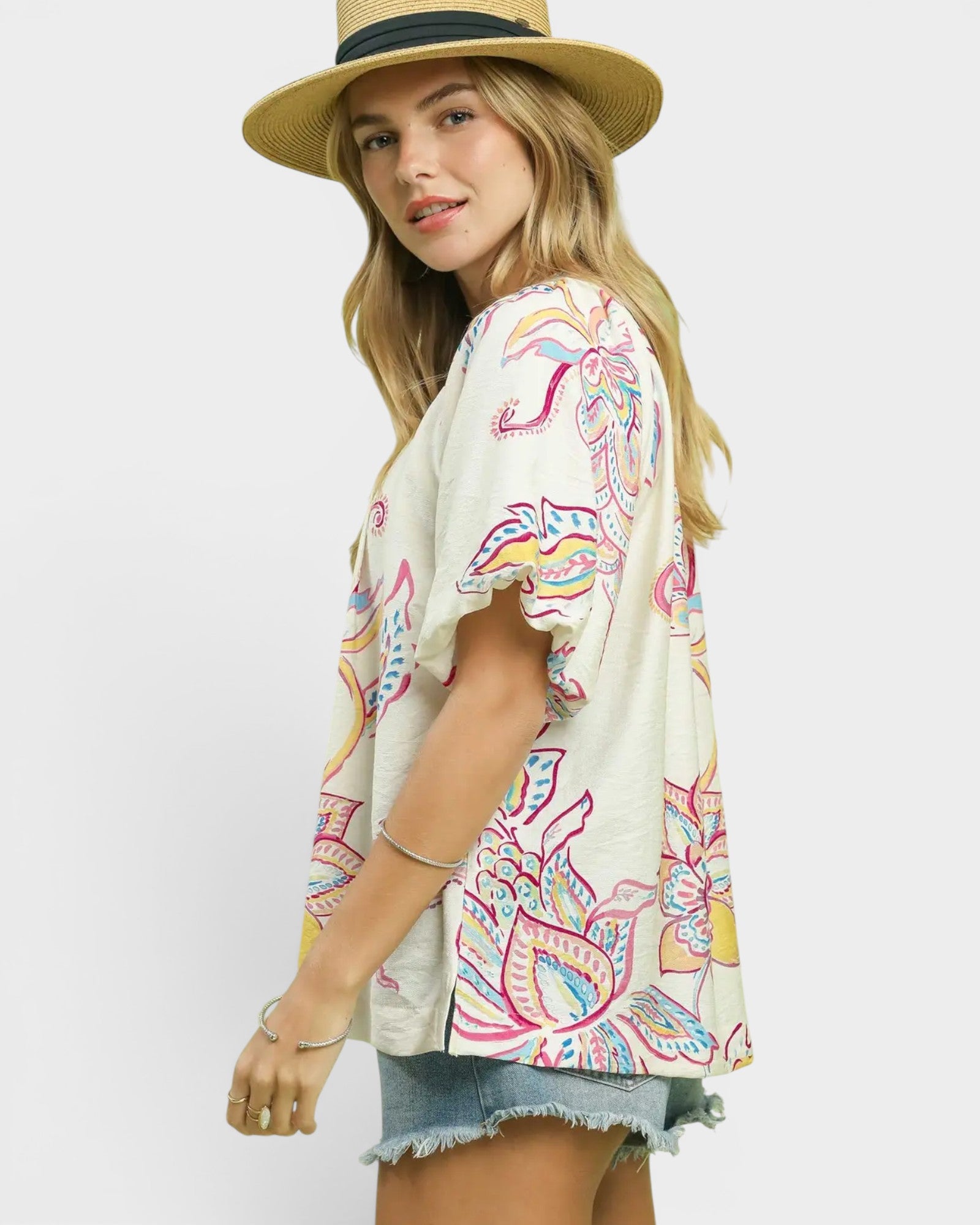 Woman wearing a colorful patterned top and straw hat on a white background