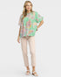 Woman wearing a green floral blouse and beige pants on a white background