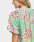Woman wearing a green blouse with colorful floral patterns on a white background