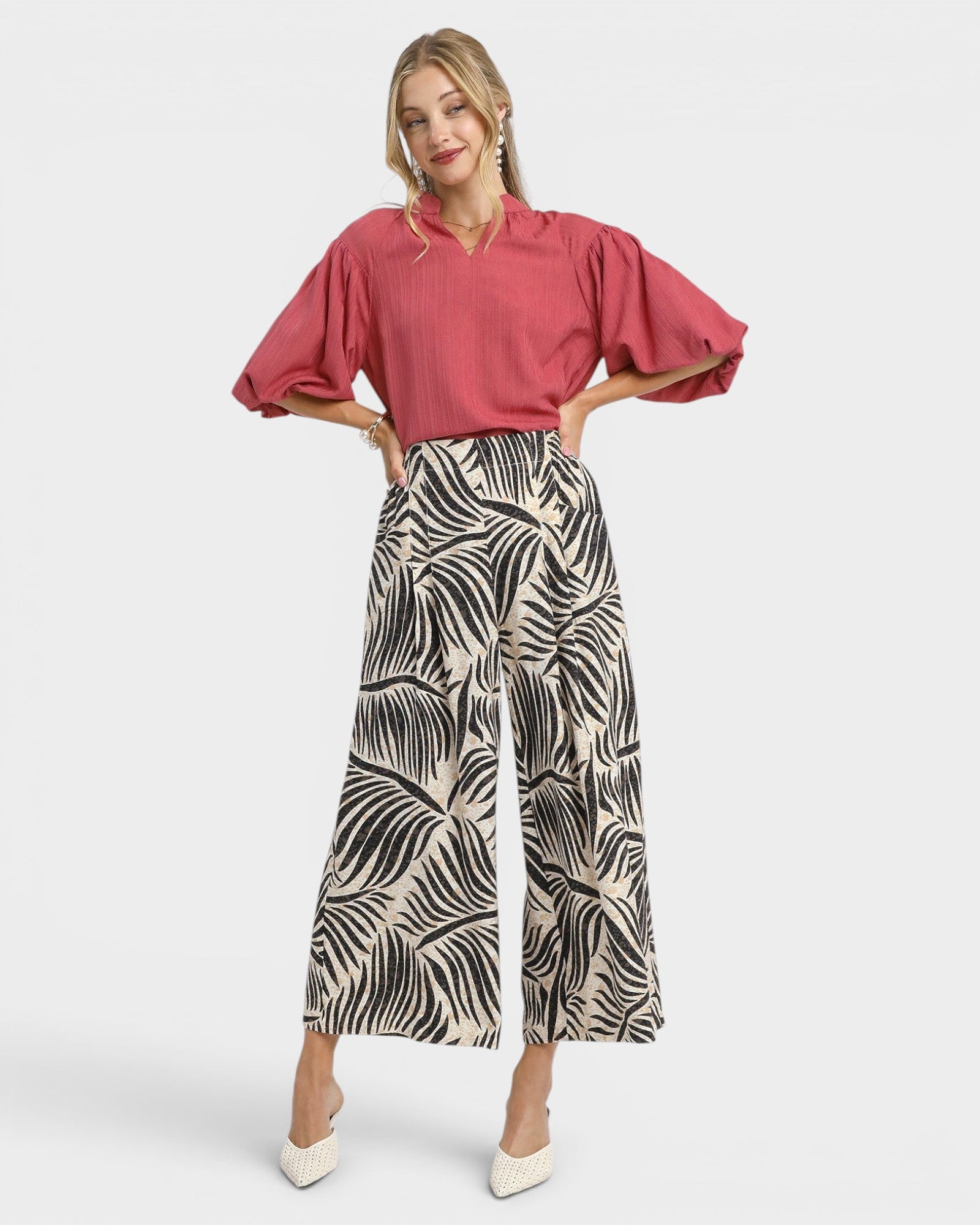 Woman wearing a pink blouse and patterned pants on a white background