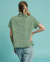 Person wearing a green patterned shirt against a light blue background