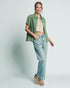 Woman wearing a green checkered shirt, beige top, and light blue jeans on a white background
