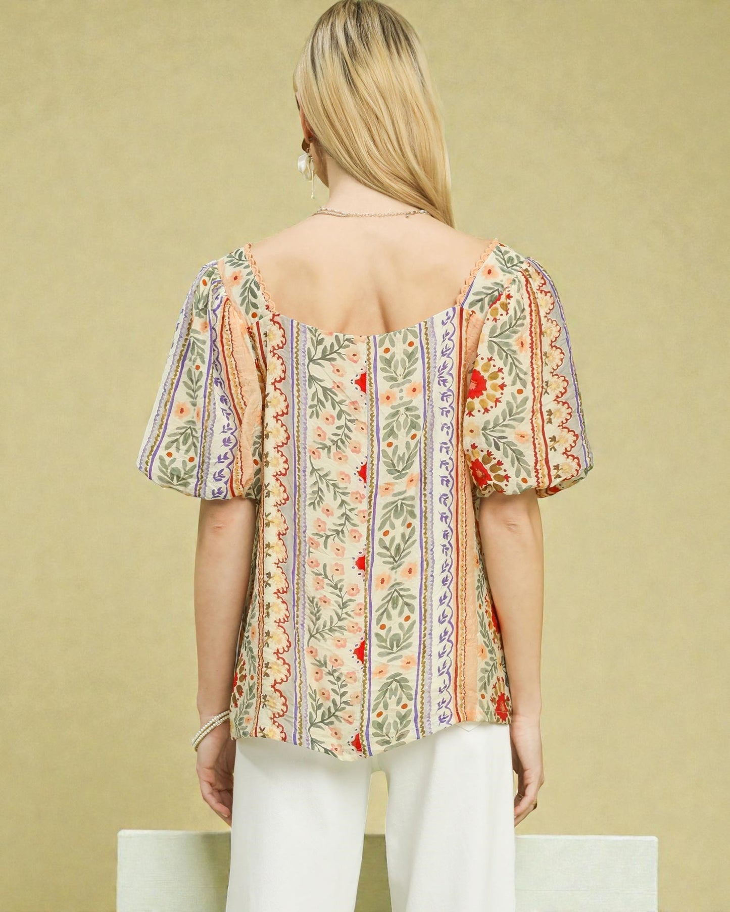 Woman wearing a floral blouse with puff sleeves against a beige background