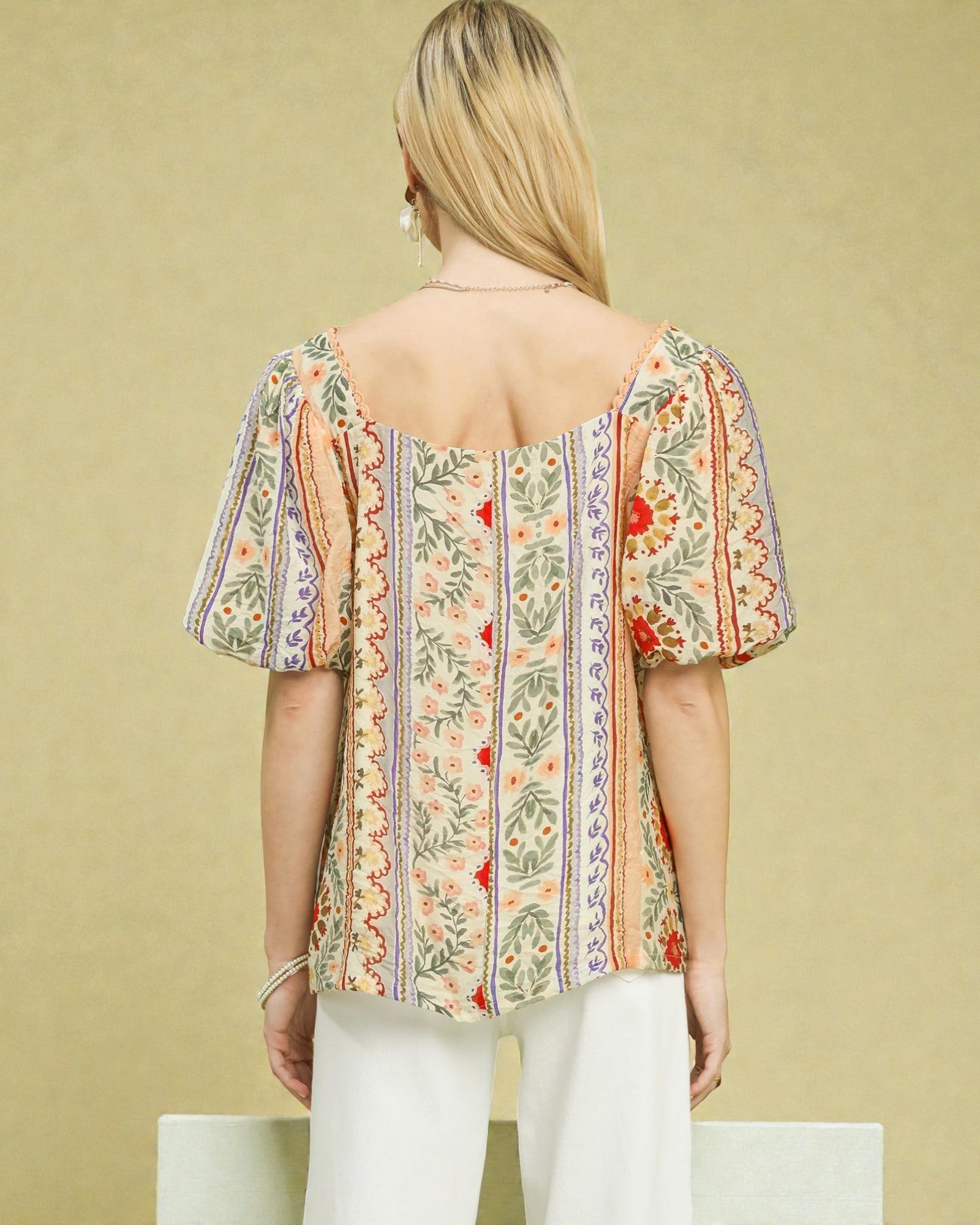 Woman wearing a floral blouse with puff sleeves against a beige background