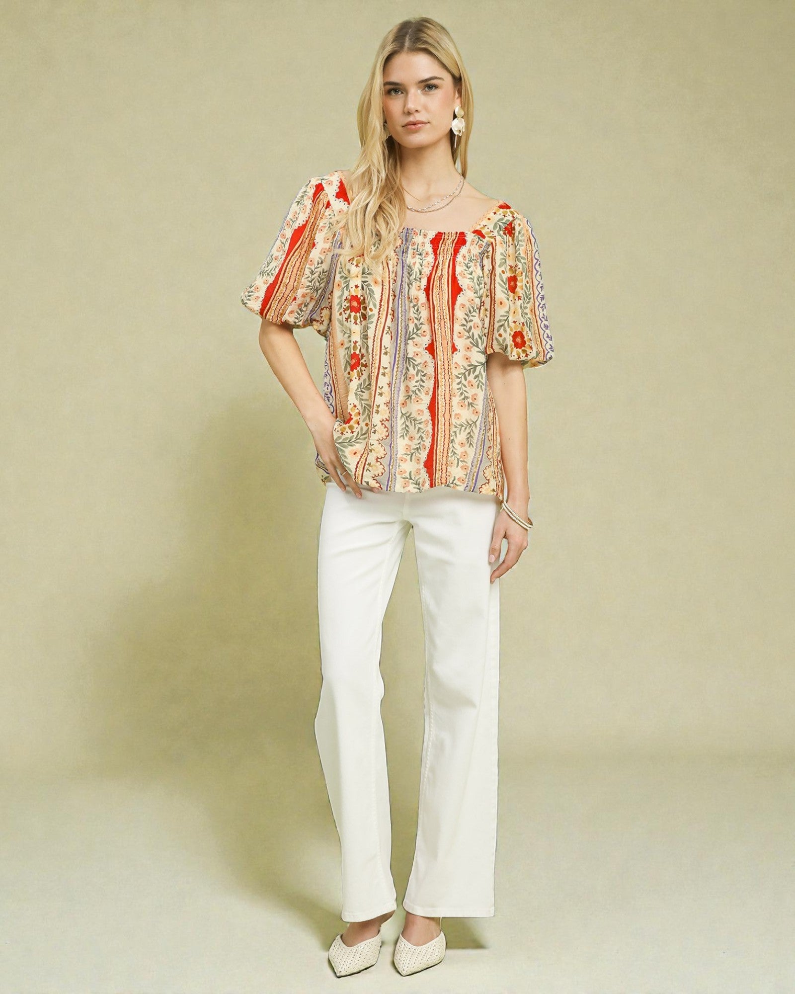 Woman wearing a patterned top and white pants against a beige background