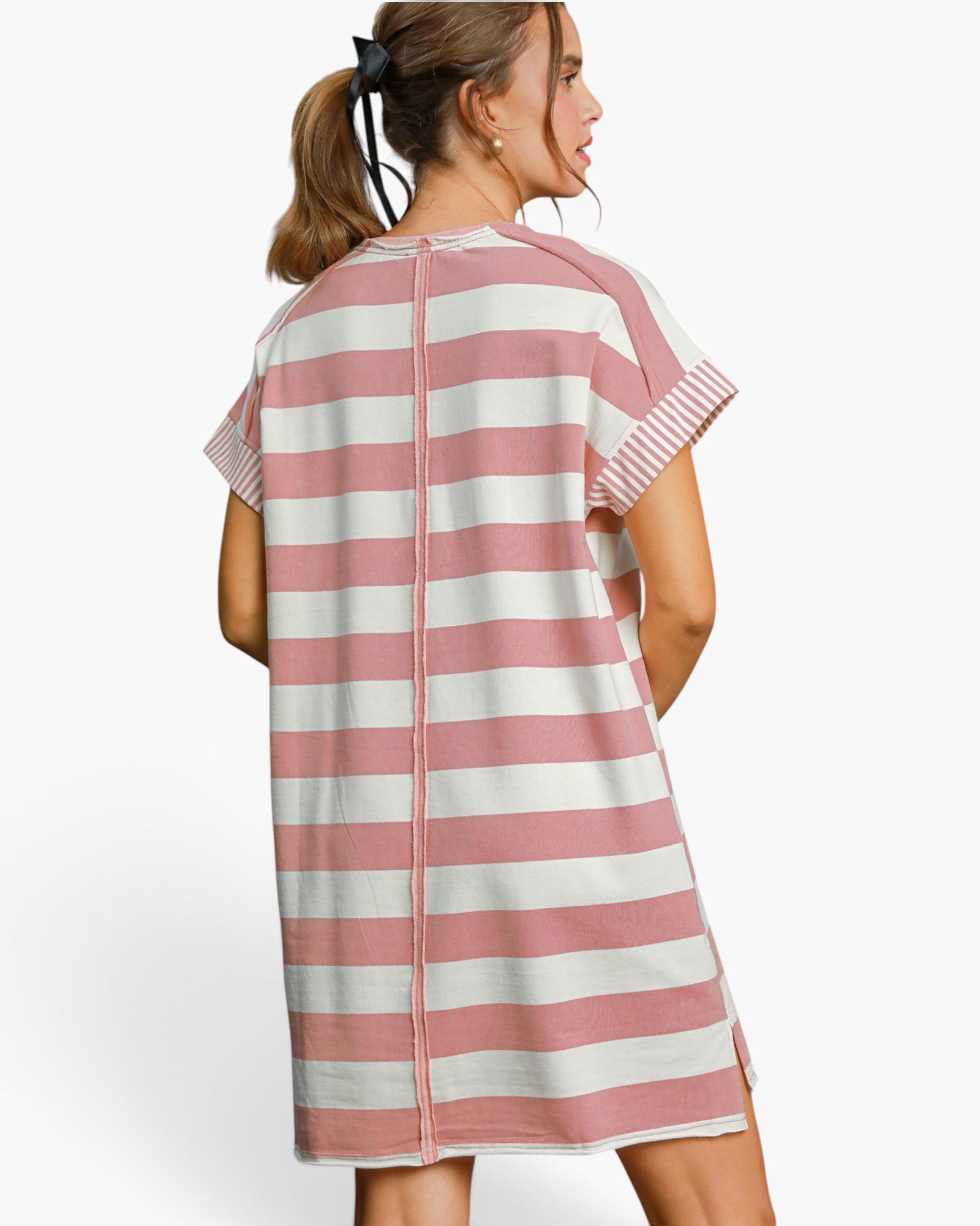 A woman shown from the back wearing a short-sleeve tunic dress with horizontal pink and off-white stripes, photographed against a clean light gray studio background.