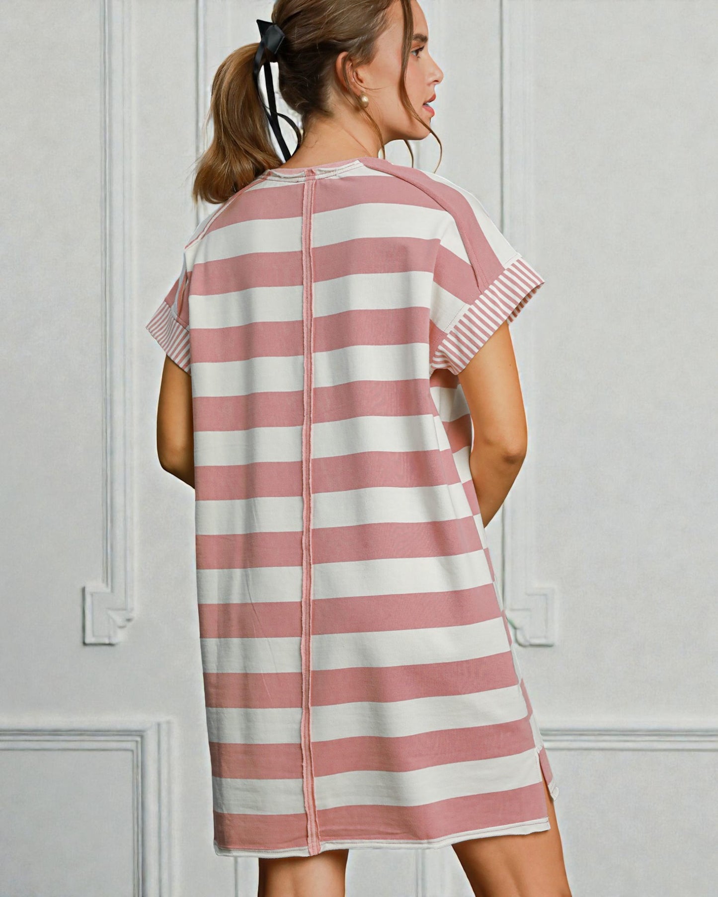 Woman wearing a pink and white striped dress against a light gray wall.