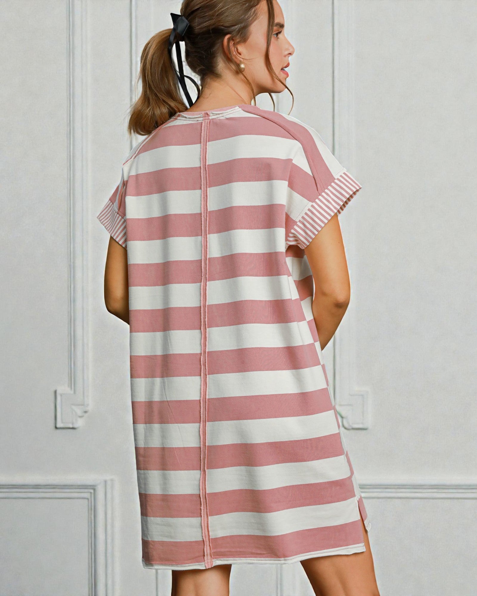 Woman wearing a pink and white striped dress against a light gray wall.
