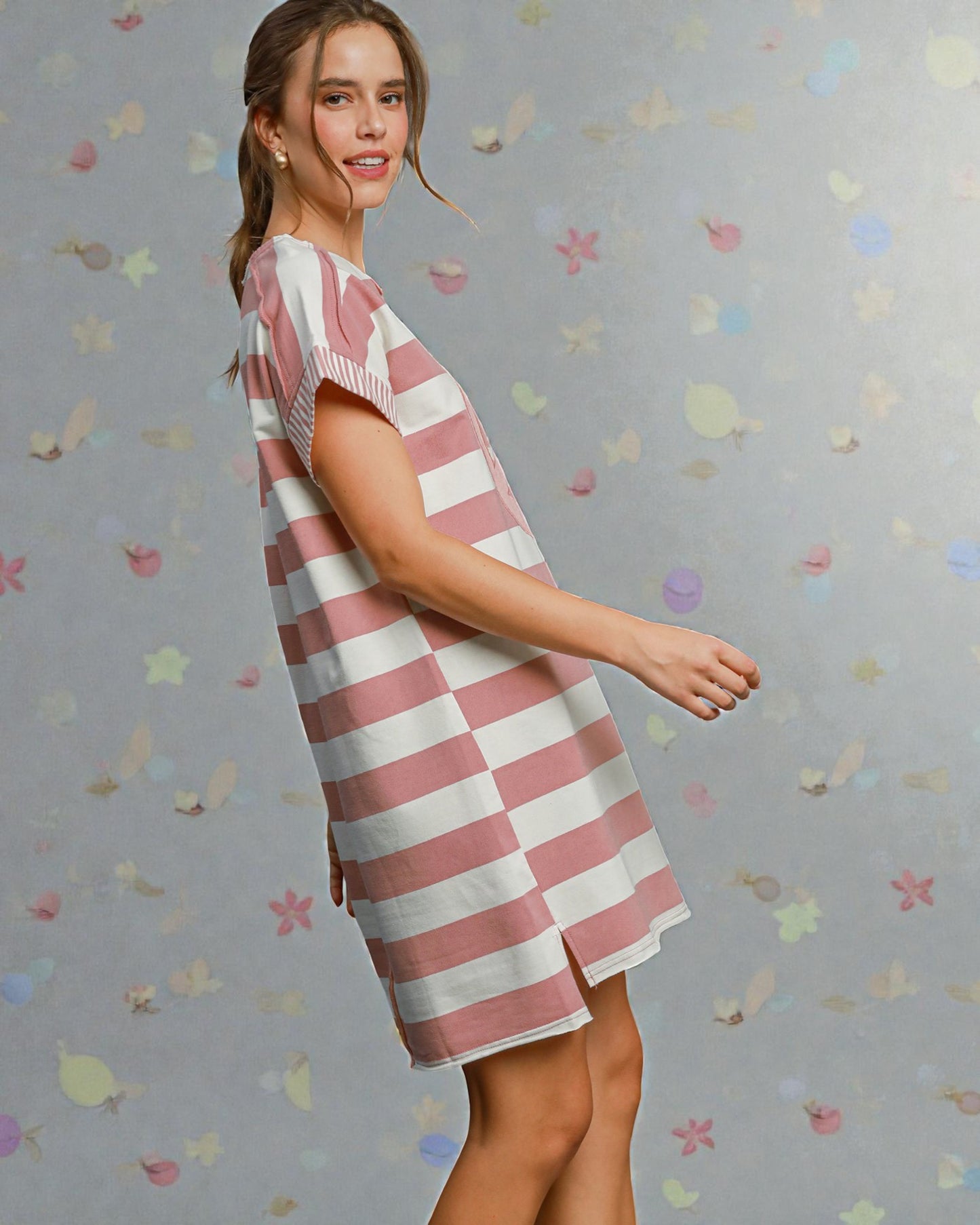 Woman wearing a pink and white striped dress against a gray background with colorful shapes.