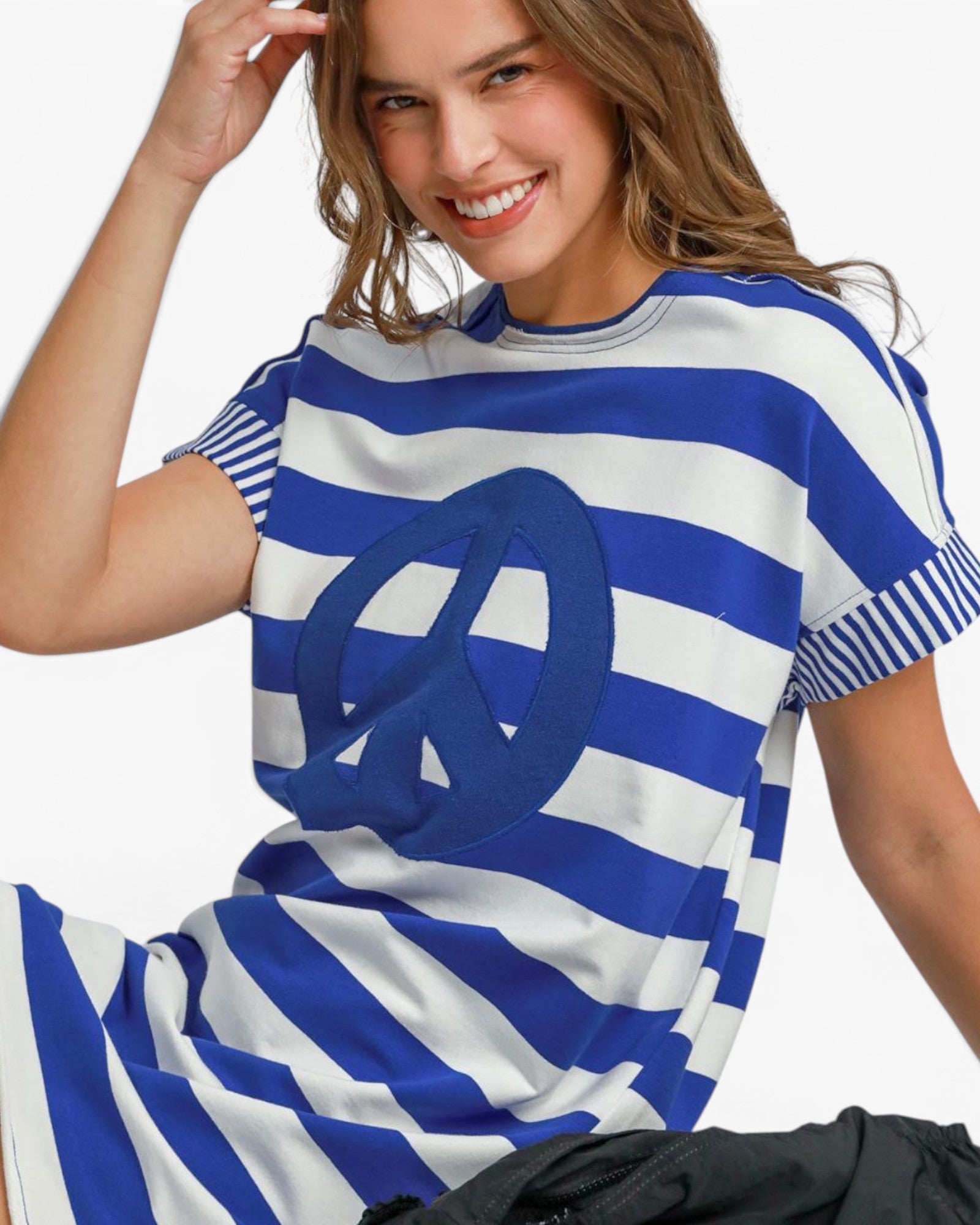 A woman wearing a blue and white striped t-shirt dress with a large blue peace sign graphic on the front, set against a plain white background.