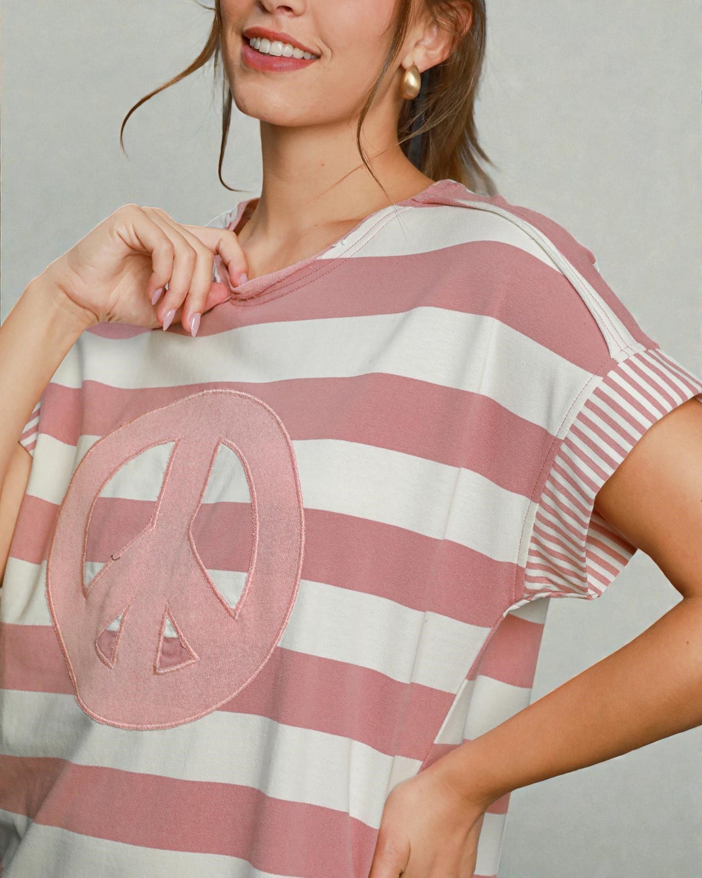 Woman wearing a pink and white striped shirt with a peace symbol design.