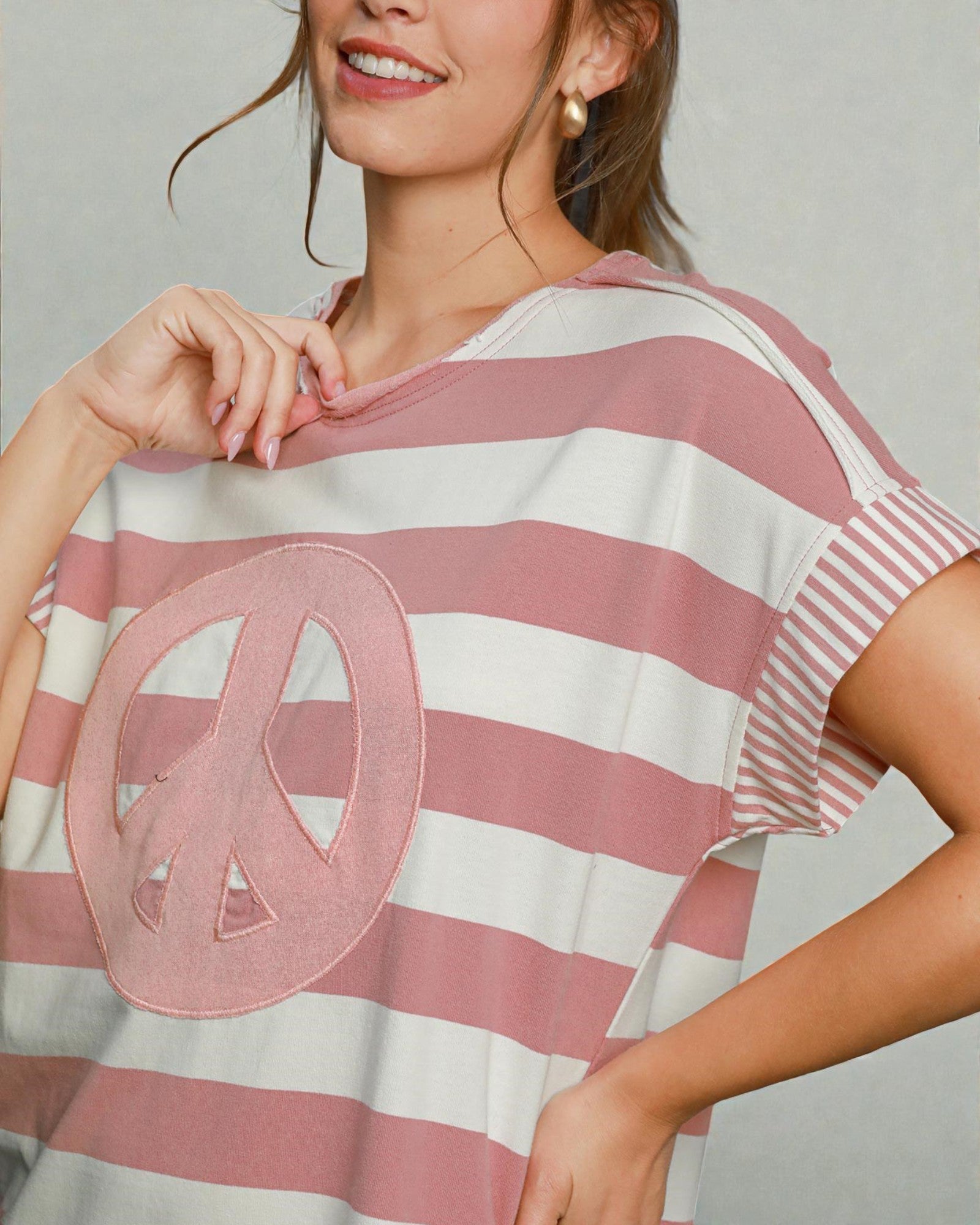 Woman wearing a pink and white striped shirt with a peace symbol design.