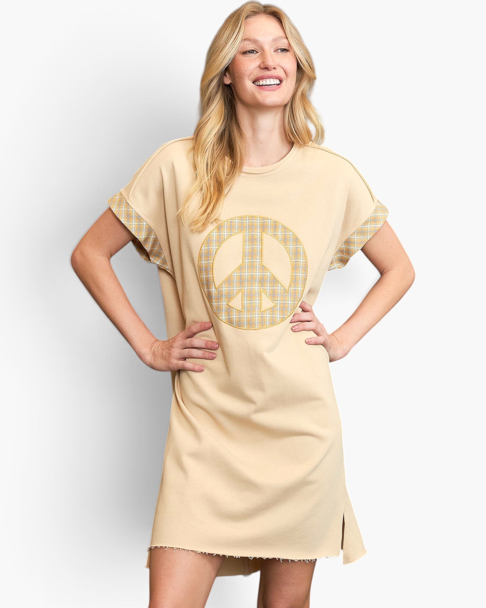 A woman modeling a beige short-sleeve t-shirt dress with a large yellow plaid peace sign graphic on the front and matching plaid cuffs.