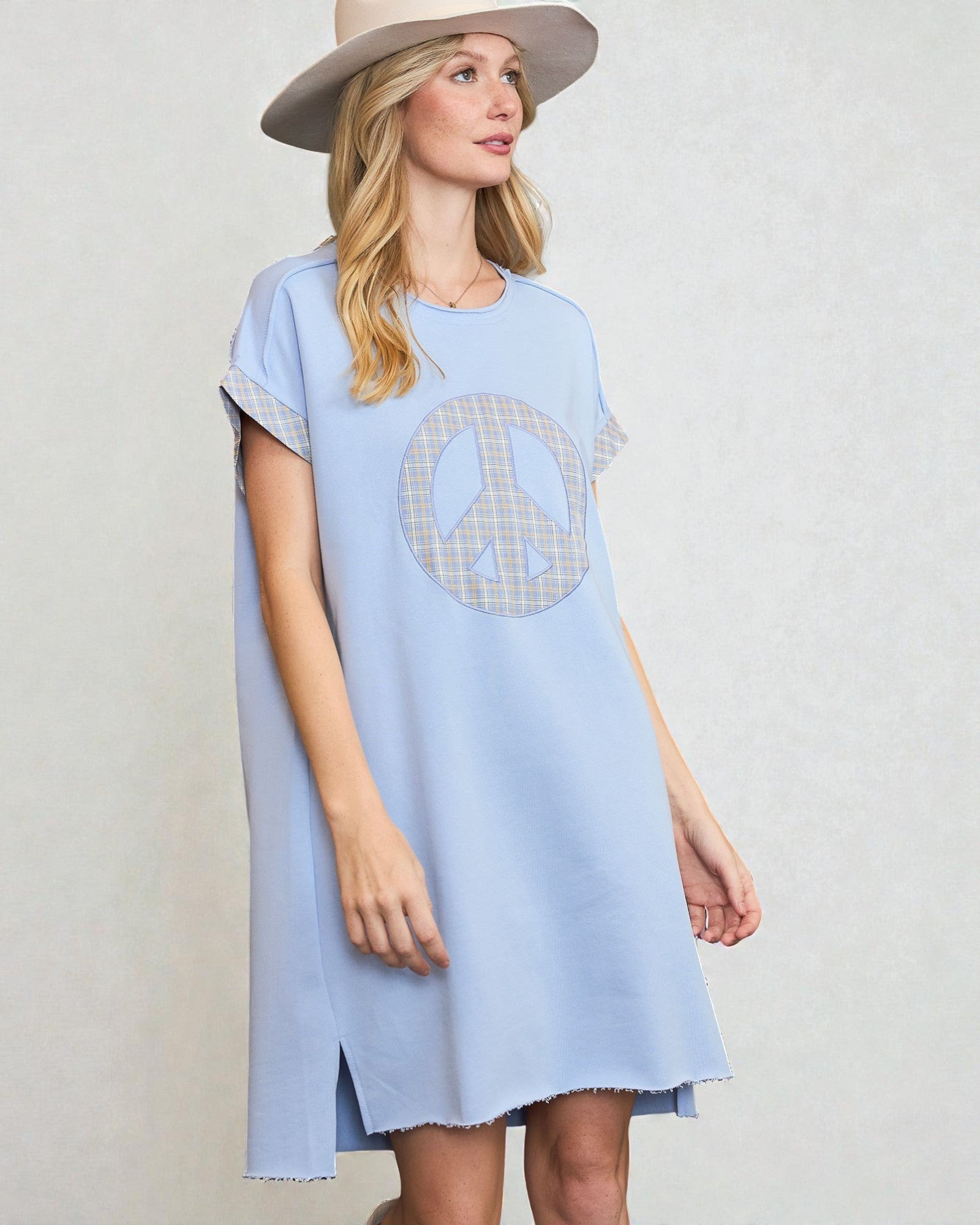 Woman wearing a light blue dress with a peace symbol design on a plain background