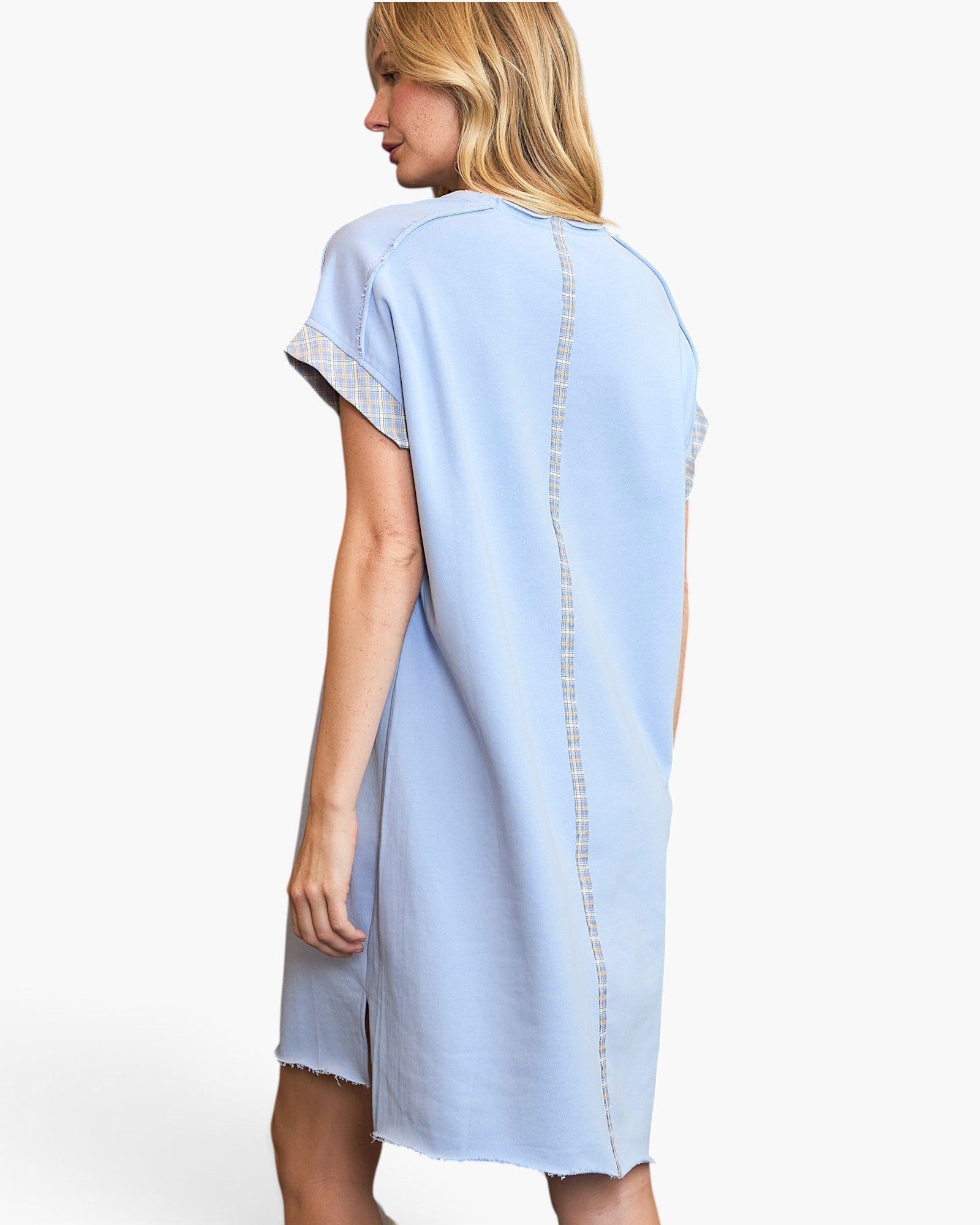 A woman shown from the back wearing a light blue short-sleeve tunic dress with decorative lace trim on the sleeves and a vertical stitched detail down the back, photographed against a plain white studio background.