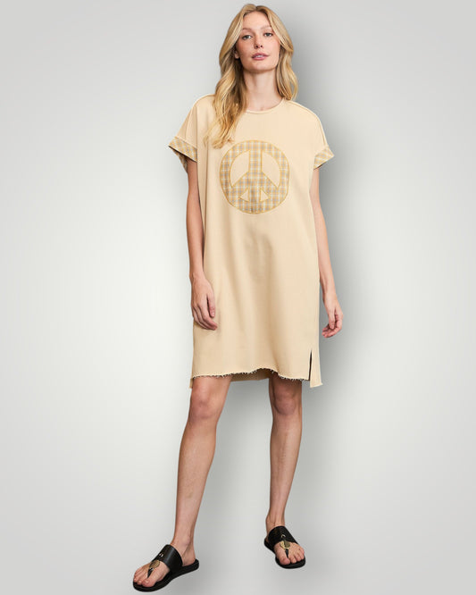 Woman wearing a beige t-shirt dress with a peace symbol design on a plain background