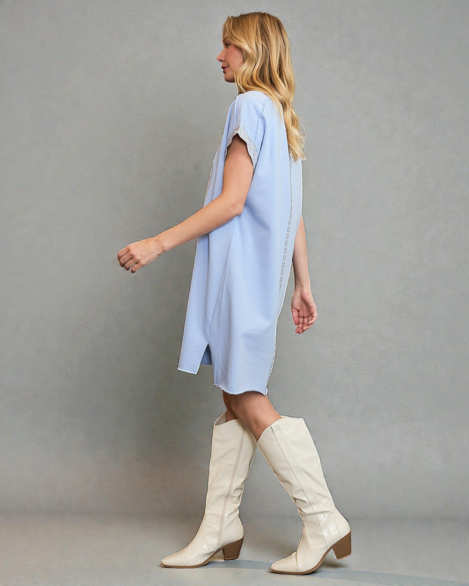 Woman wearing a light blue dress and white knee-high boots against a gray background