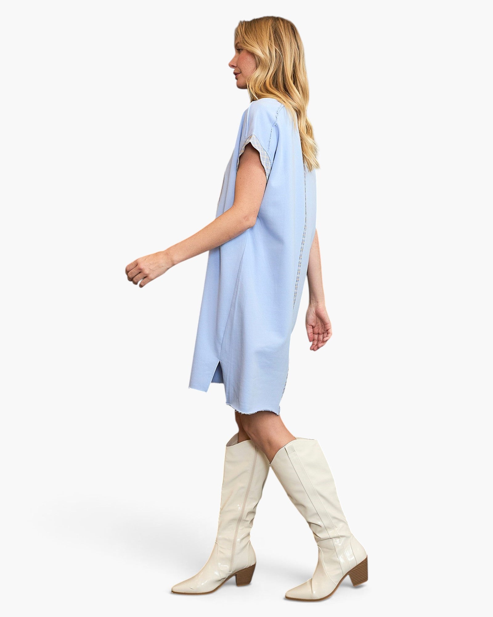 A woman modeling a light blue short-sleeve shift dress with white knee-high heeled boots against a plain white studio background.