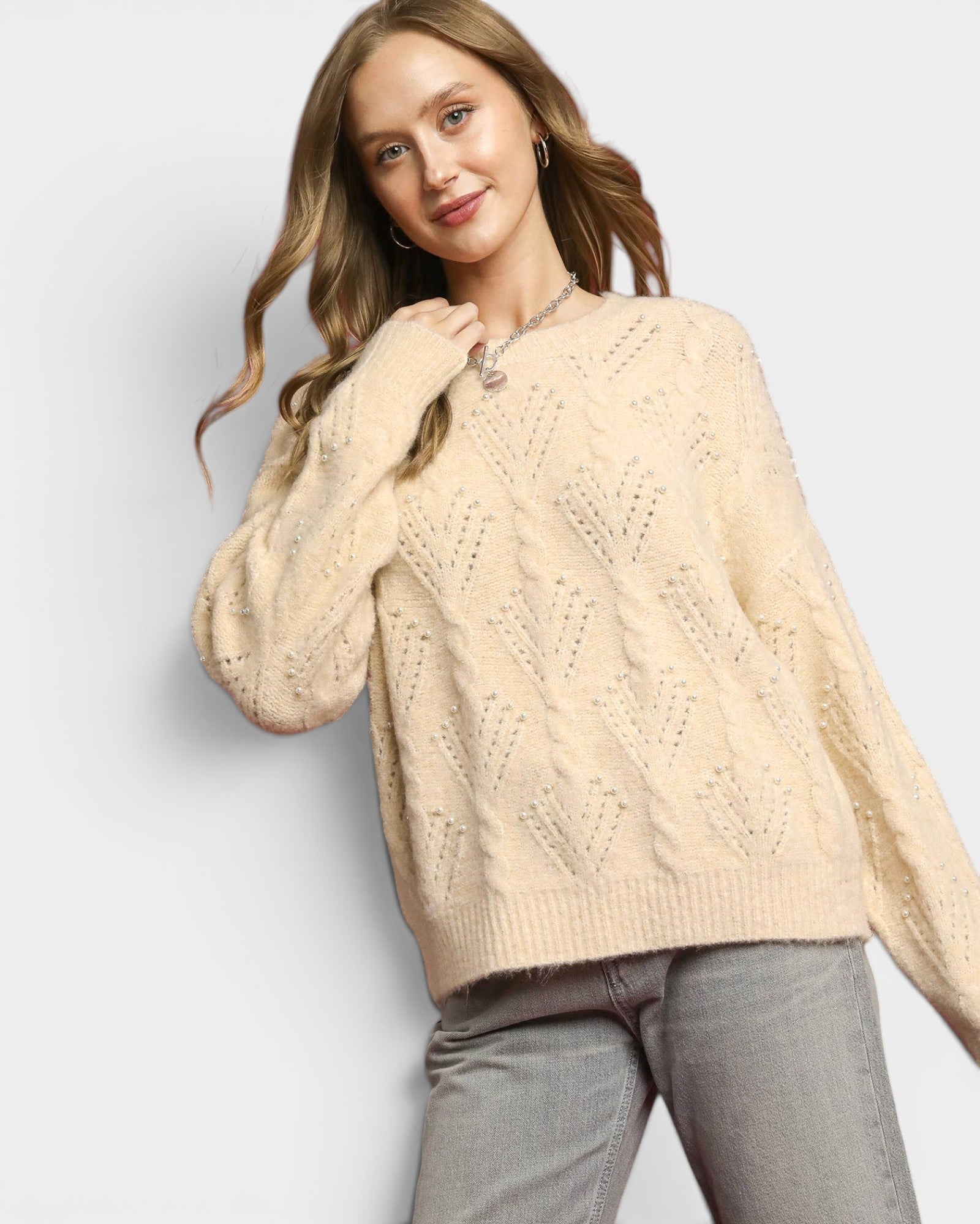 Woman wearing a beige cable knit sweater on a light gray background