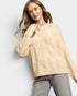 Woman wearing a beige cable knit sweater on a light gray background
