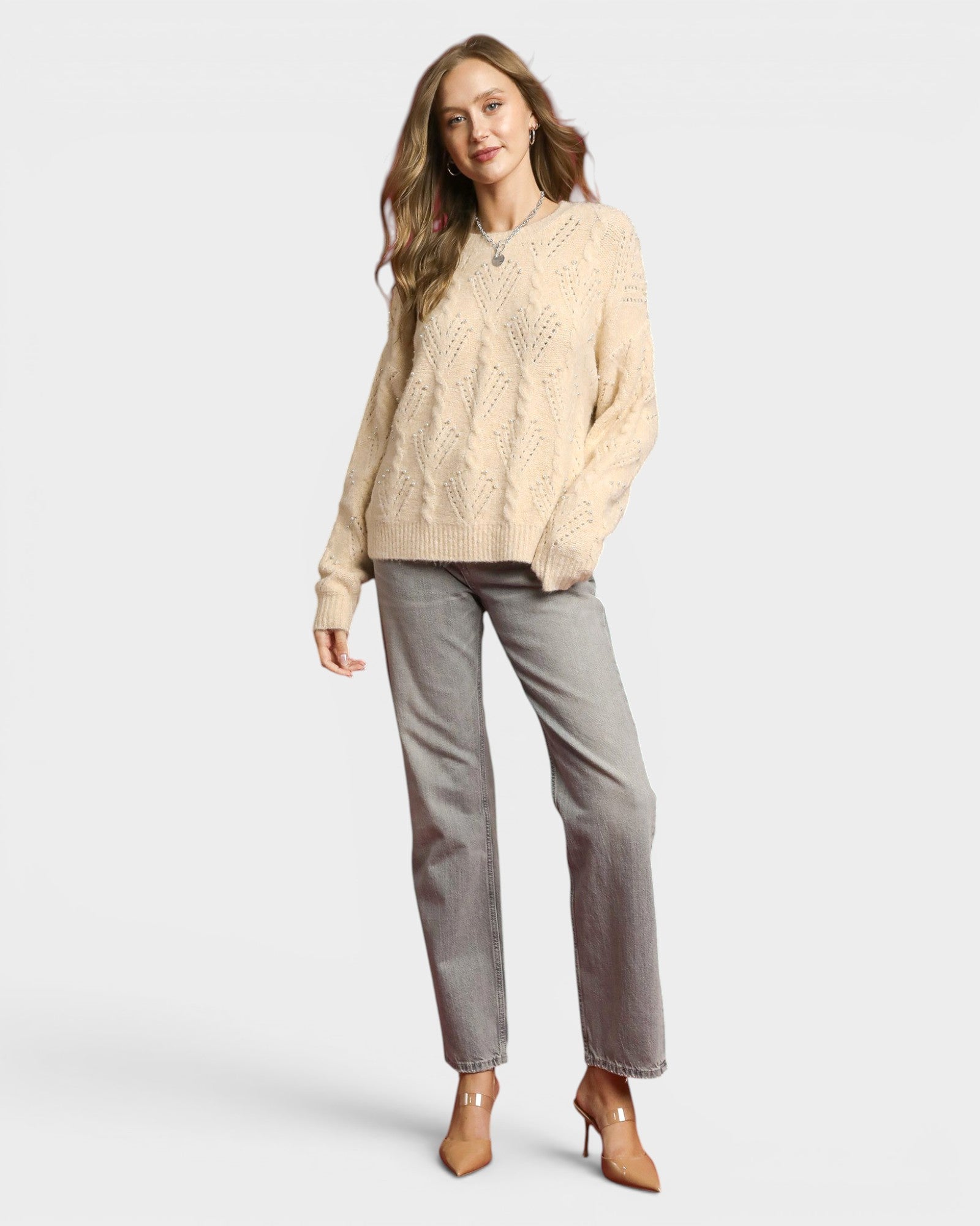 Woman wearing a beige cable knit sweater and gray pants on a white background