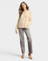 Woman wearing a beige cable knit sweater and gray pants on a white background
