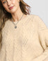 Close-up of a person wearing a beige sweater with a textured pattern on a light background