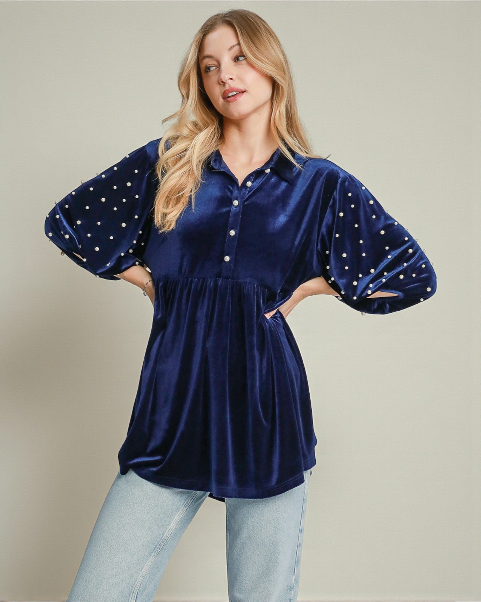 Woman wearing a blue velvet blouse with star patterns on sleeves against a beige background