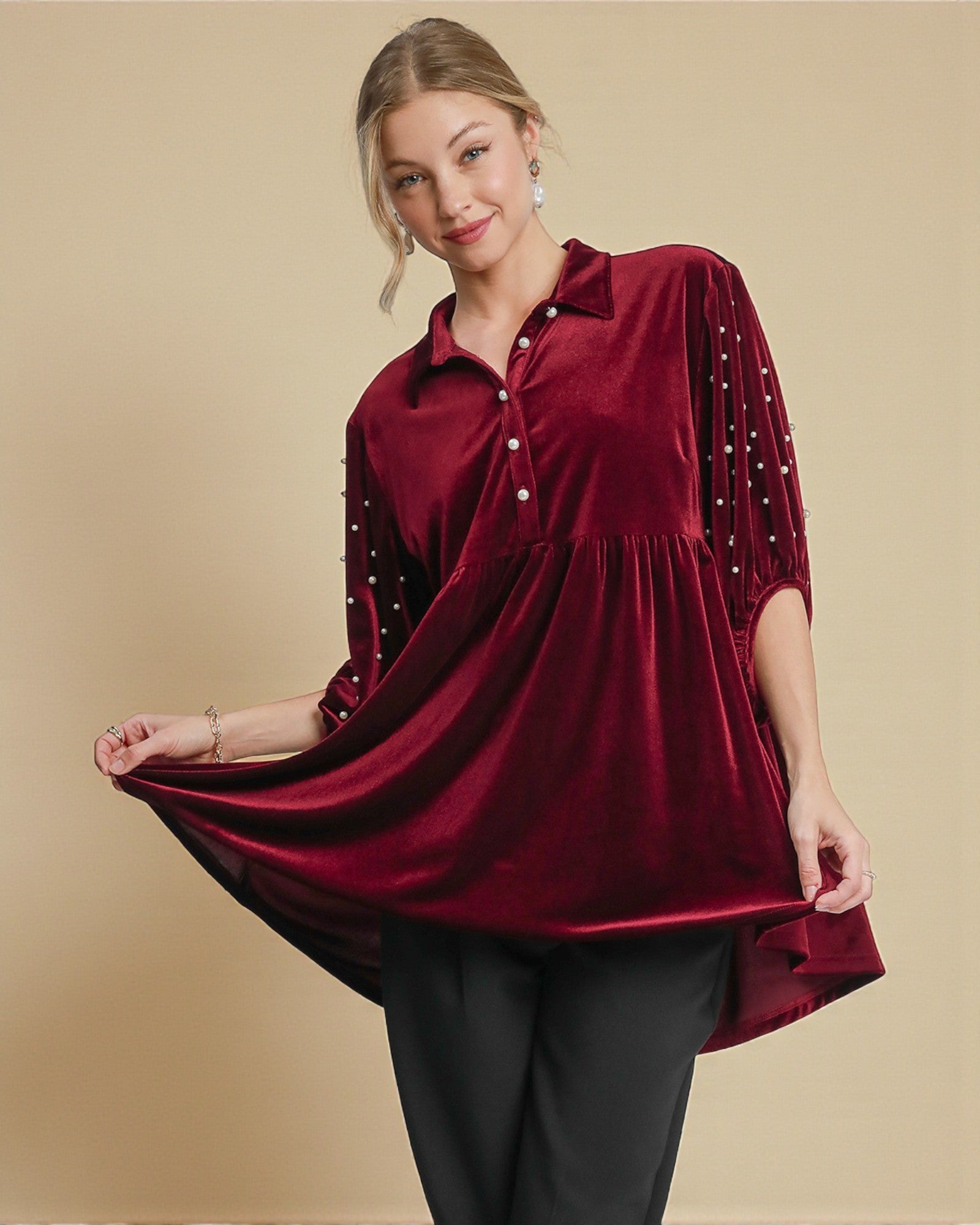 Woman wearing a burgundy velvet top with black trim on a beige background