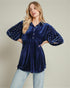 Woman wearing a blue velvet blouse with star patterns on sleeves against a beige background