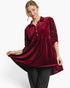 A woman modeling a deep burgundy velvet tunic top with three-quarter sleeves, adorned with small pearl-like embellishments along the sleeve edges, paired with black pants against a clean white studio background.