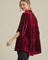 Woman wearing a burgundy velvet dress with sheer sleeves on a beige background