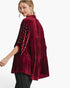 A woman wearing a deep burgundy velvet tiered tunic top with embellished sleeves, photographed from a three-quarters back angle against a plain white studio background.