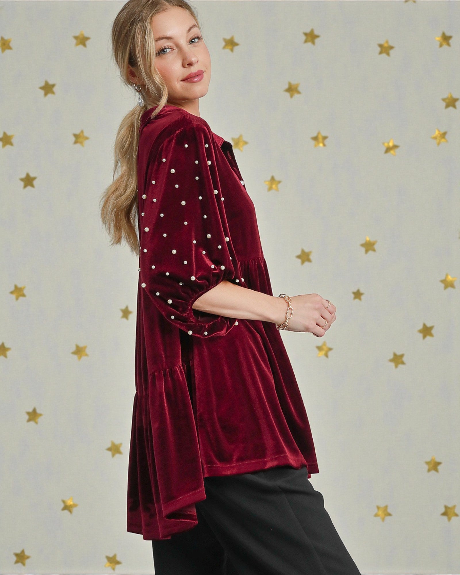Woman wearing a burgundy velvet jacket with pearl embellishments against a star-patterned background