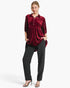 A woman modeling a burgundy velvet long-sleeve top with silver rhinestone embellishments on the sleeves, paired with black pants and black heeled sandals, against a light gray studio background.