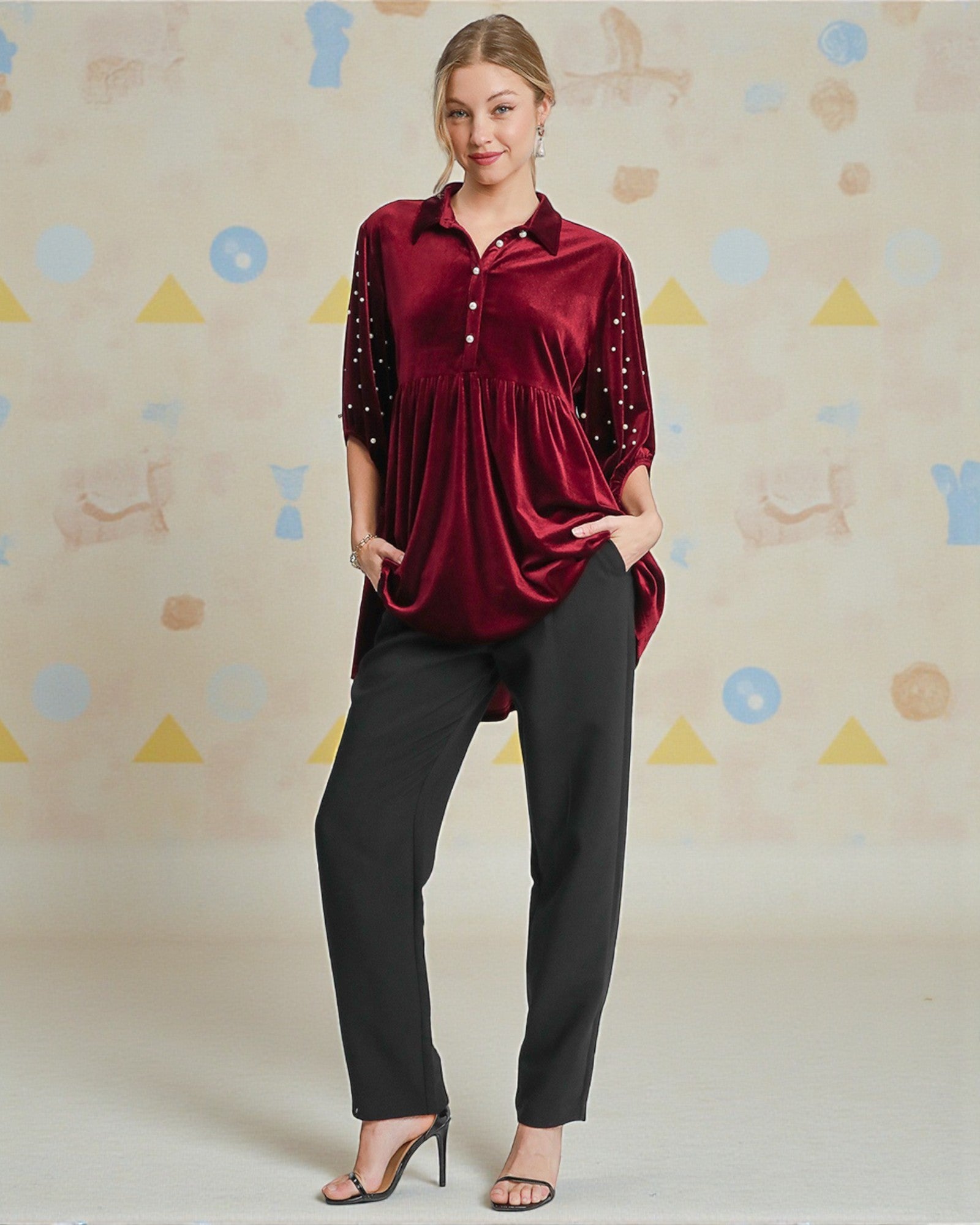 Woman wearing a red blouse with black embellishments and black pants against a patterned background