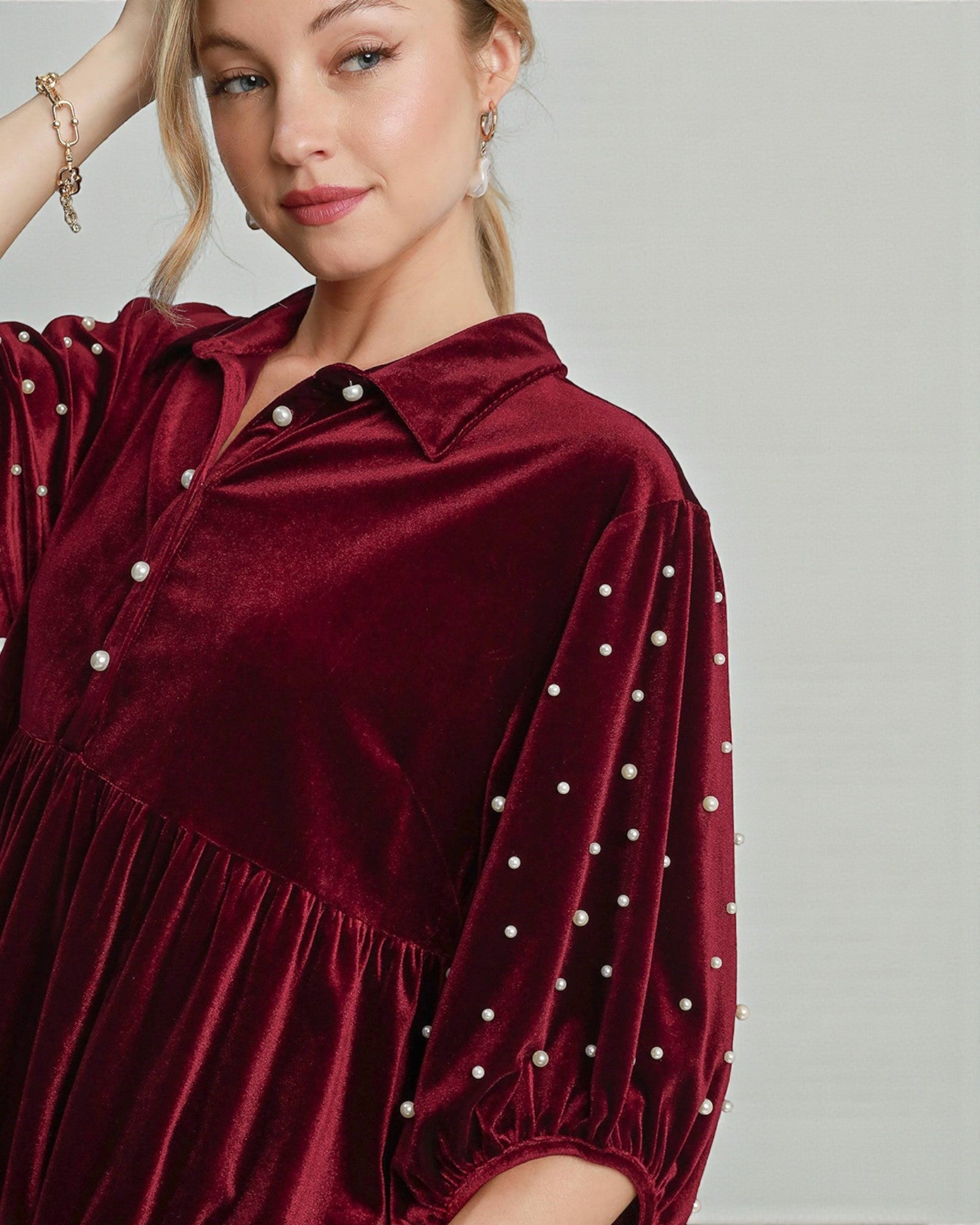 Woman wearing a burgundy velvet dress with pearl embellishments on a plain background