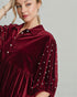 Woman wearing a burgundy velvet dress with pearl embellishments on a plain background
