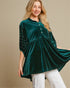 Woman wearing a green velvet top with pearl embellishments on a beige background
