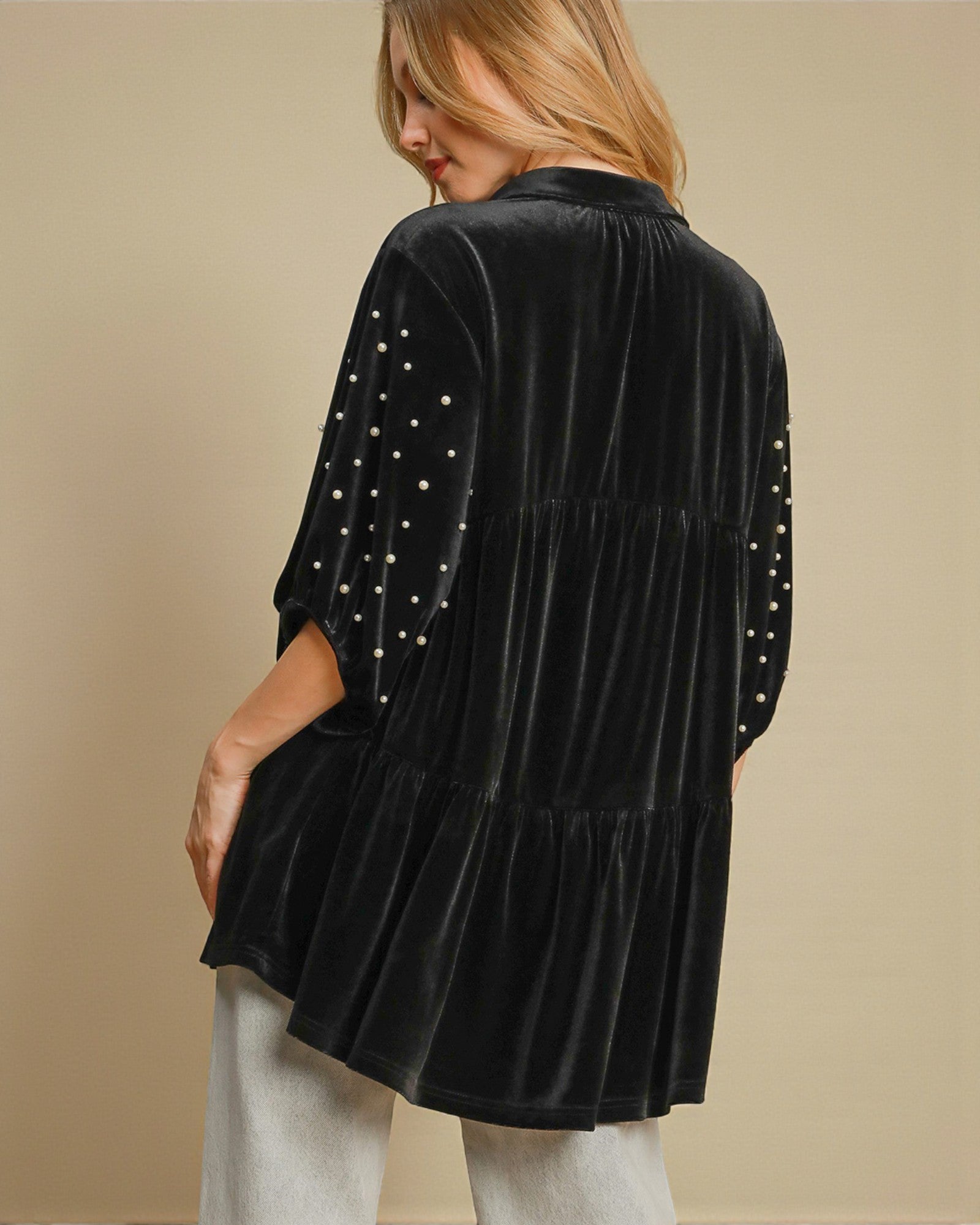 Black velvet jacket with pearl embellishments worn by a person on a beige background