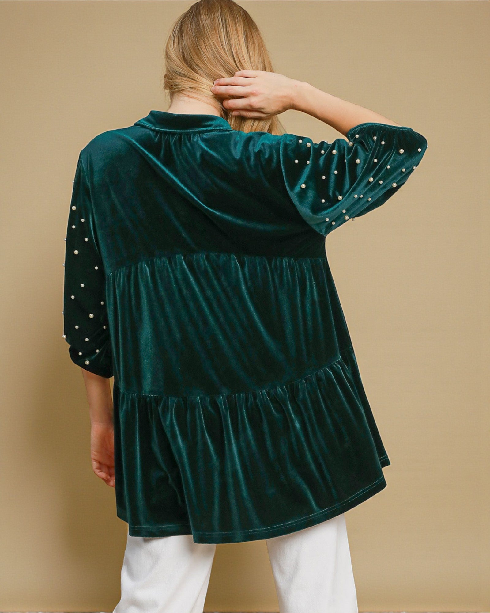 Green velvet top with white polka dots on sleeves against a beige background