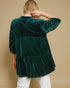 Green velvet top with white polka dots on sleeves against a beige background